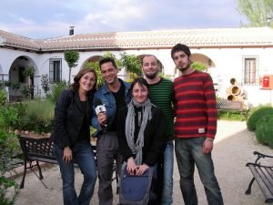 La directora del hotel, Ángela Jiménez Egea, posa sonriente sujetando el micrófono junto al presentador del programa Andalucía Directo, Jesús Toral y su equipo de cámaras y operadores. Detrás se ve el jardín del hotel con sus arcos blancos y su fuente de tinajas.