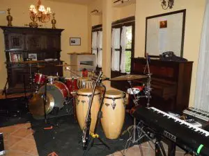 El salón del hotel está transformado en estudio de grabación. A la derecha se encuentran los teclados de Noni, en el centro los bongos de Alfredo y al fondo la batería con sus parabenes. Todo ello alrededor del piano y el aparador del salón.